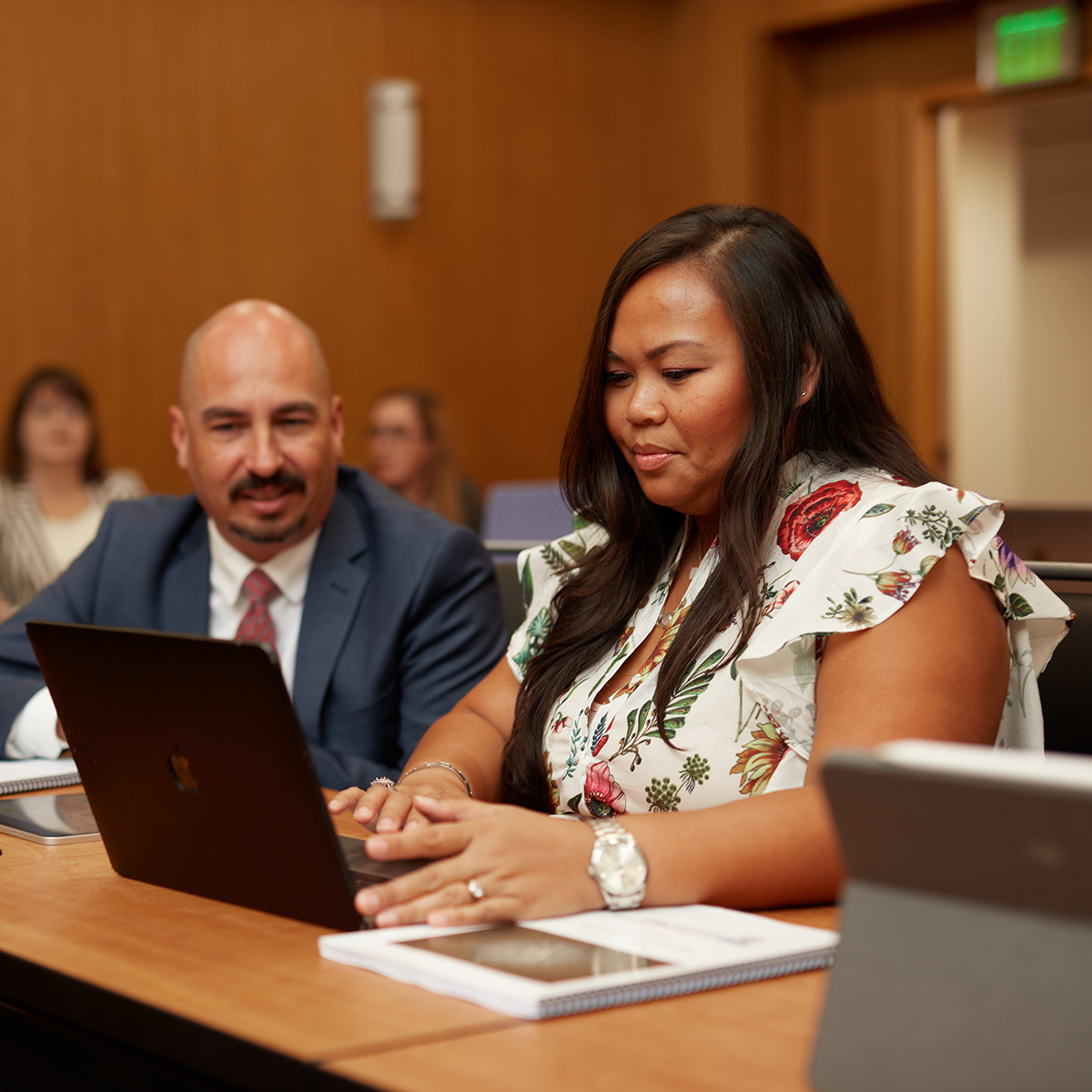 Two students in professional attire sitting at a desk, collaborating on a computer.